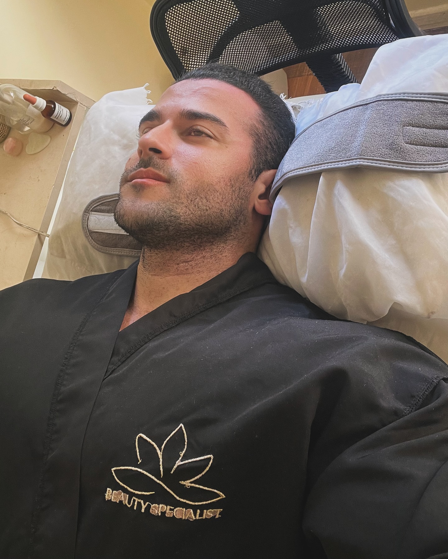 Un cliente recostado en la camilla facial con la bata negra de Beauty Specialist, con el loto dorado bordado